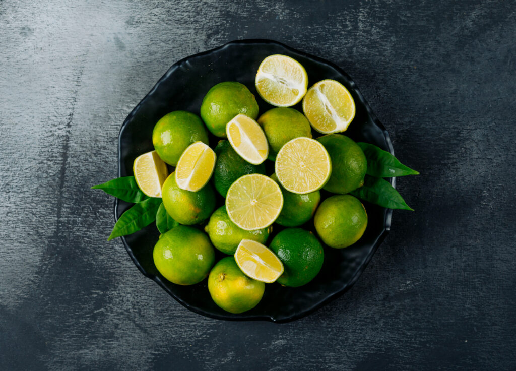 green lemons plate with slices top view black textured background