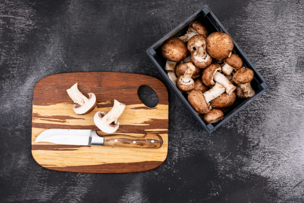sliced mushroom with knife wooden cutting board near wooden box with fresh mushrooms