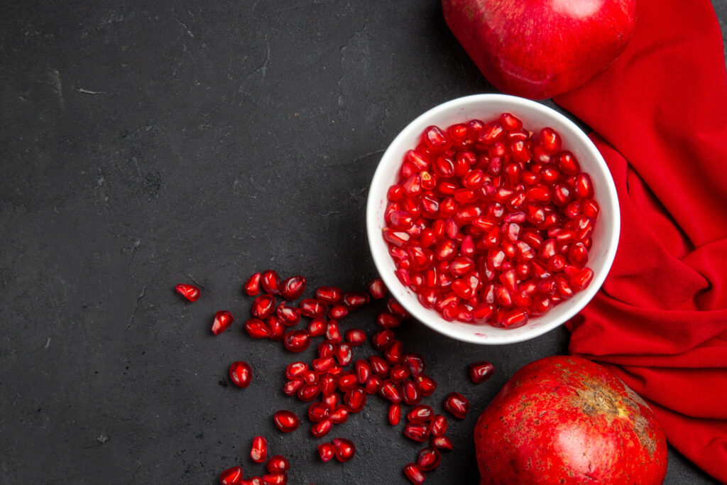 top close up view pomegranate two pomegranates pomegranate seeds bowl red tablecloth