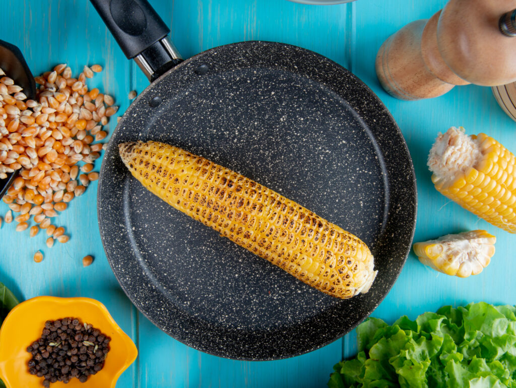 top view corn cob pan with corn seeds black pepper seeds cut corn lettuce around blue surface