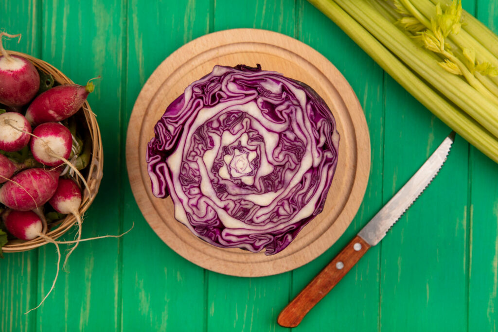 top view purple cabbage wooden kitchen board with knife with radishes bucket with celery isolated green wooden wall