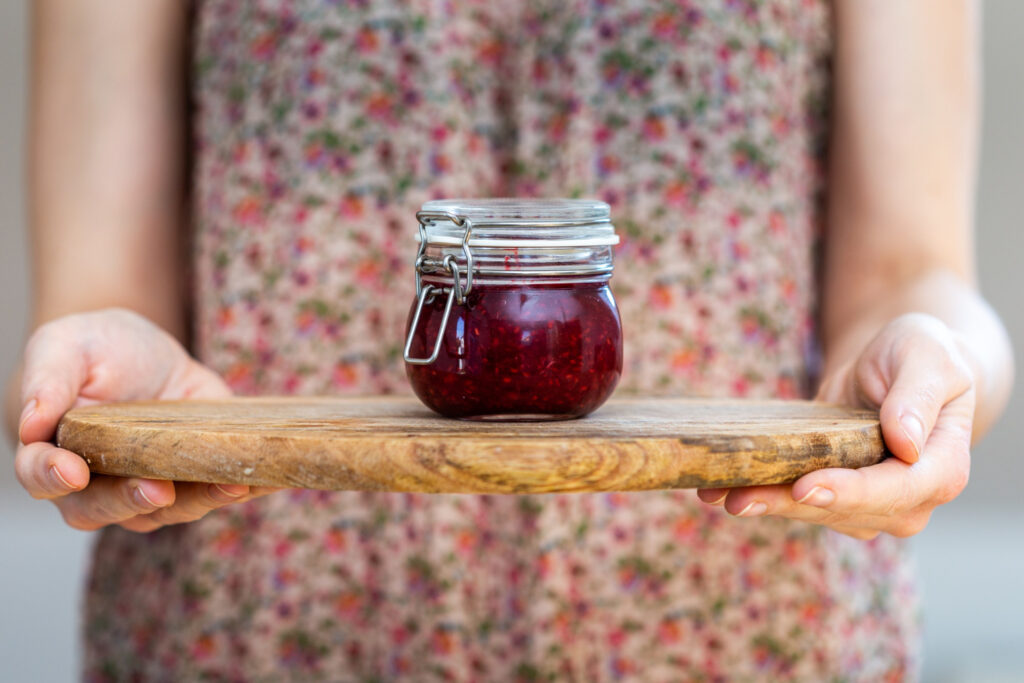 woman holding homemade vegan raw raspberry jam glass jar wooden surface