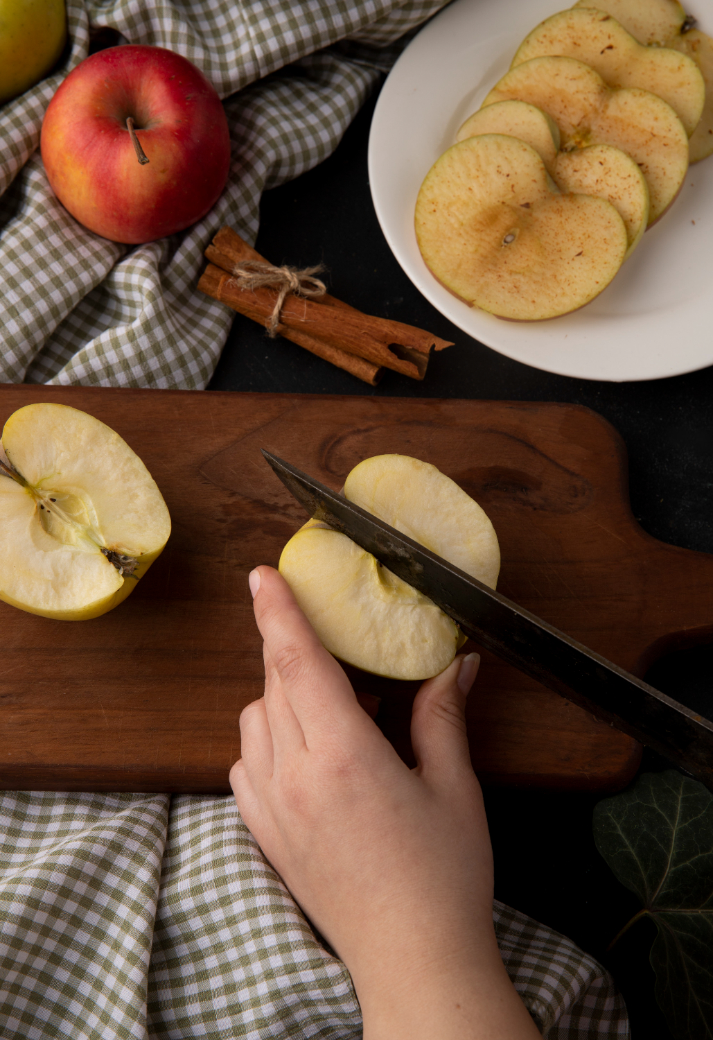 side view woman cuts yellow apple board with cinnamon apple slices plate checkered tablecloth